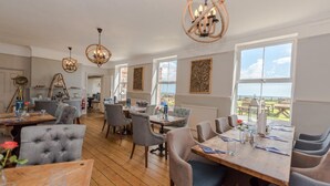 A dining area with wooden tables and chairs, chandeliers, and a view of the outdoors. - The Ship Inn (Norwich)