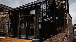 A rustic building with a black exterior and a sign reading "The Catch at the Ship Inn". - The Ship Inn (Norwich)