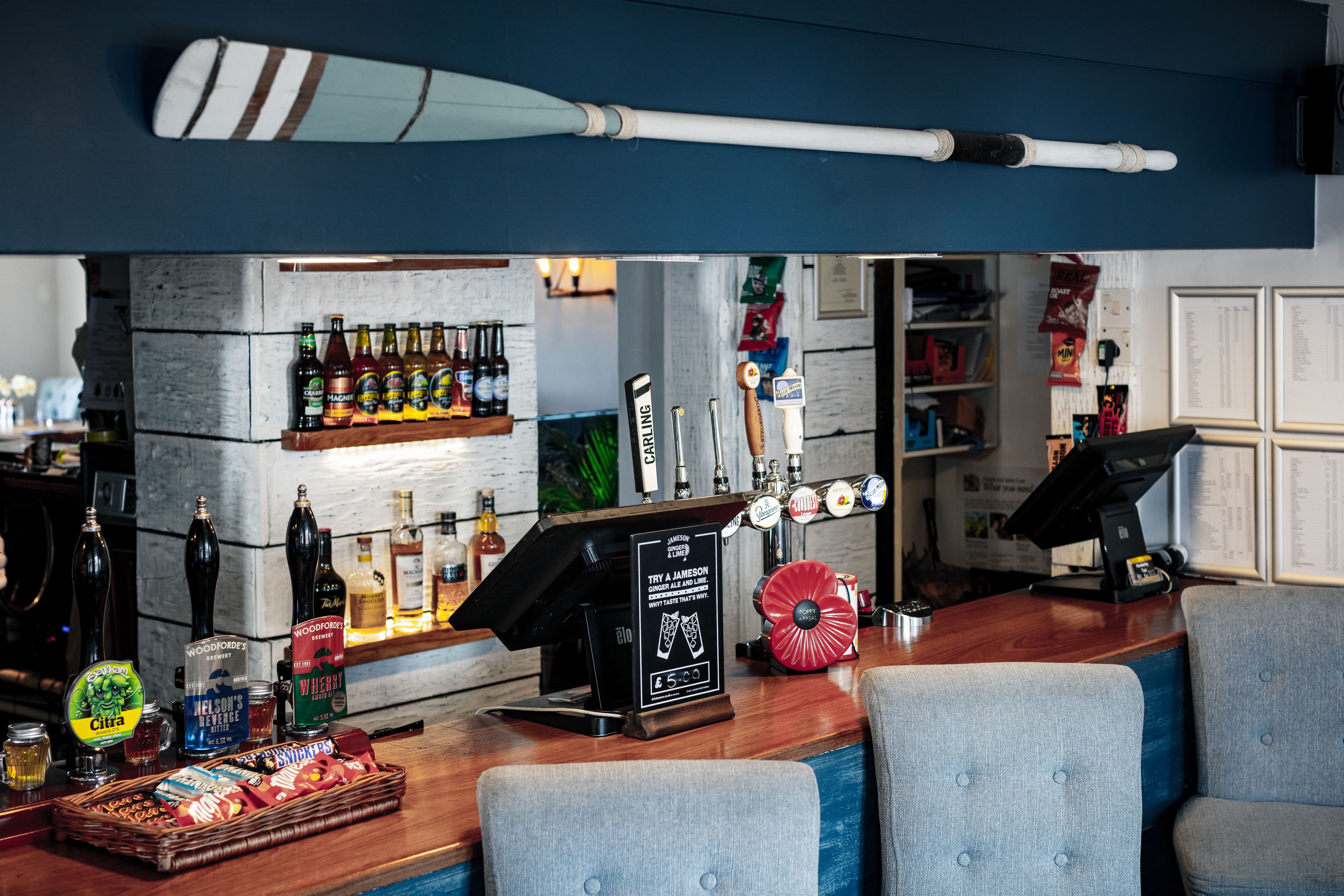 A bar area with a wooden counter, various bottles, a cash register, and seating.