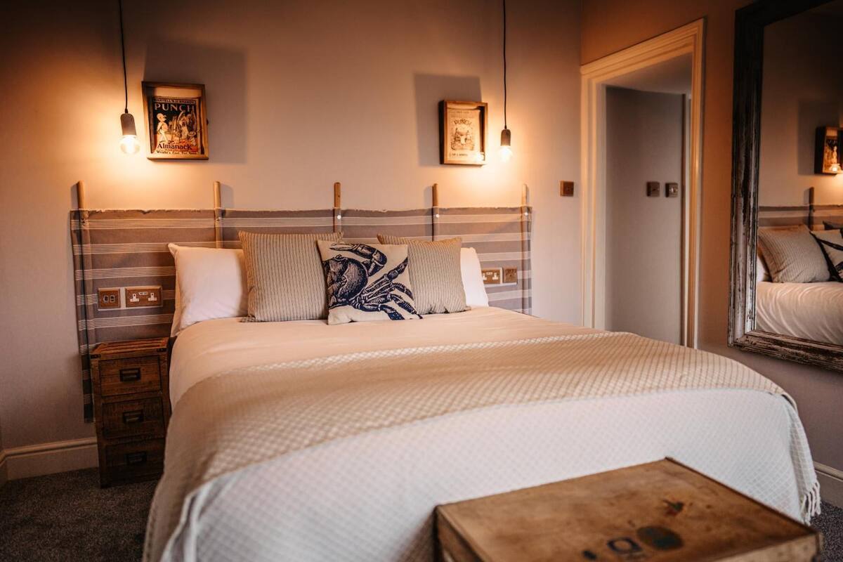 A neatly made bed with a striped headboard, two bedside lamps, and a small wooden chest of drawers.