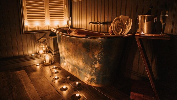 A vintage bathtub with a towel, a wine glass, and a candle on a wooden floor. - The Ship Inn (Norwich)