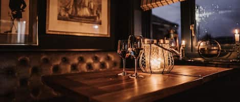Un coin bar avec une table en bois, deux verres, un chandelier et des œuvres d’art encadrées accrochées au mur.