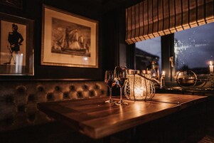 Una zona de bar con una mesa de madera, dos vasos, un candelabro y obras de arte enmarcadas en la pared.
