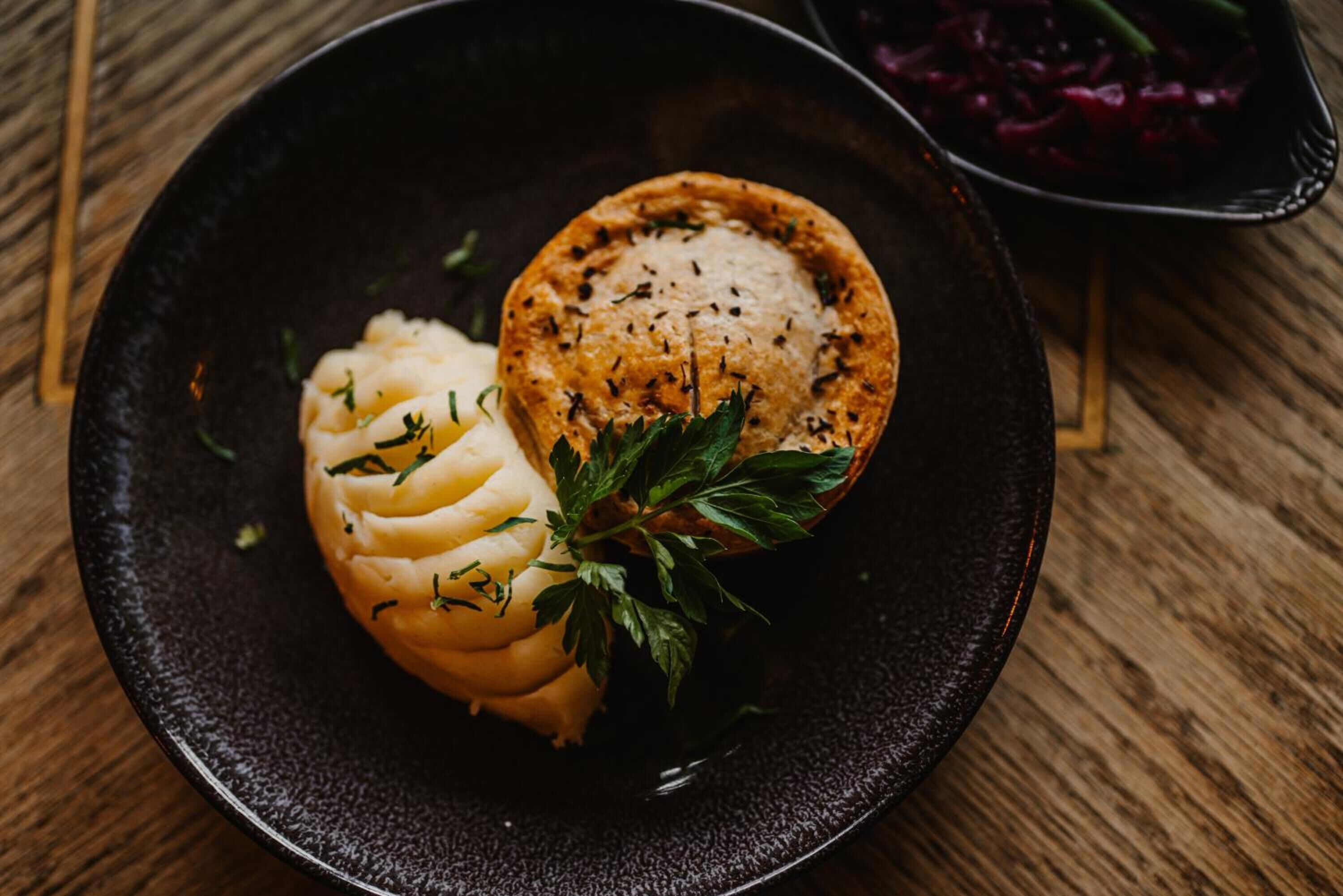 A dish with mashed potatoes and a meat pie on a dark plate.