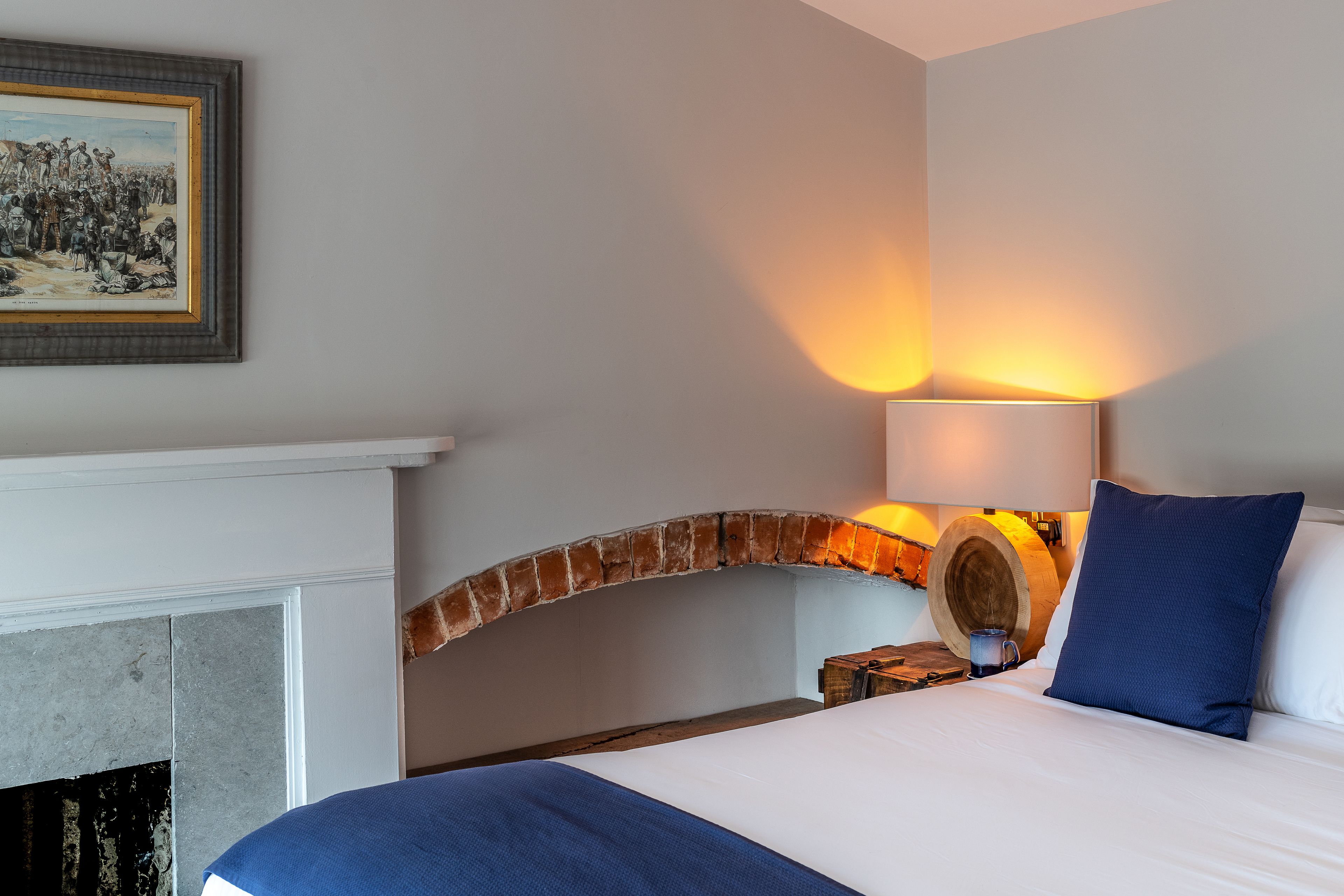 Una habitación de hotel con una cama, una chimenea, una lámpara y un cuadro en la pared.