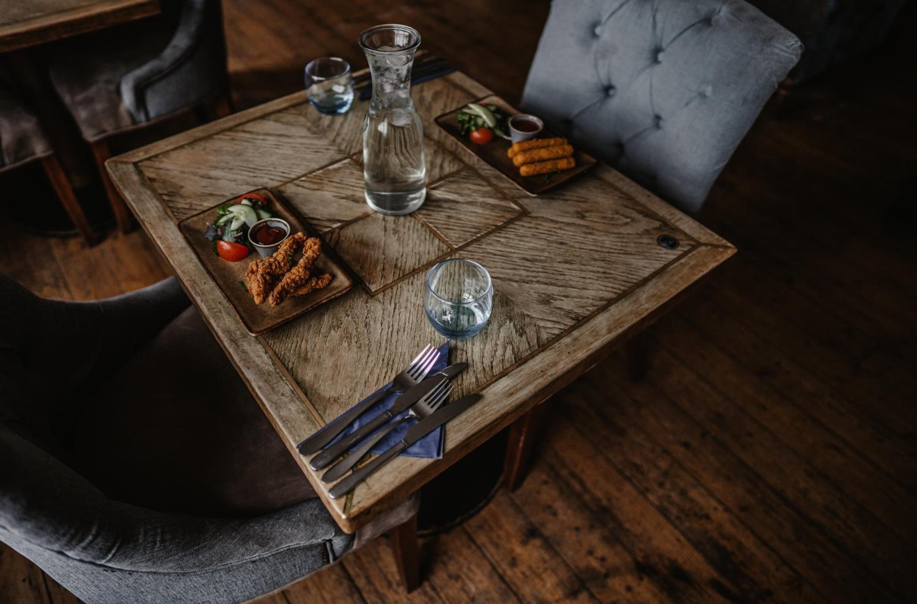 Een houten tafel met een bord gefrituurd kippenvlees, een waterkan en een klein glas water.
