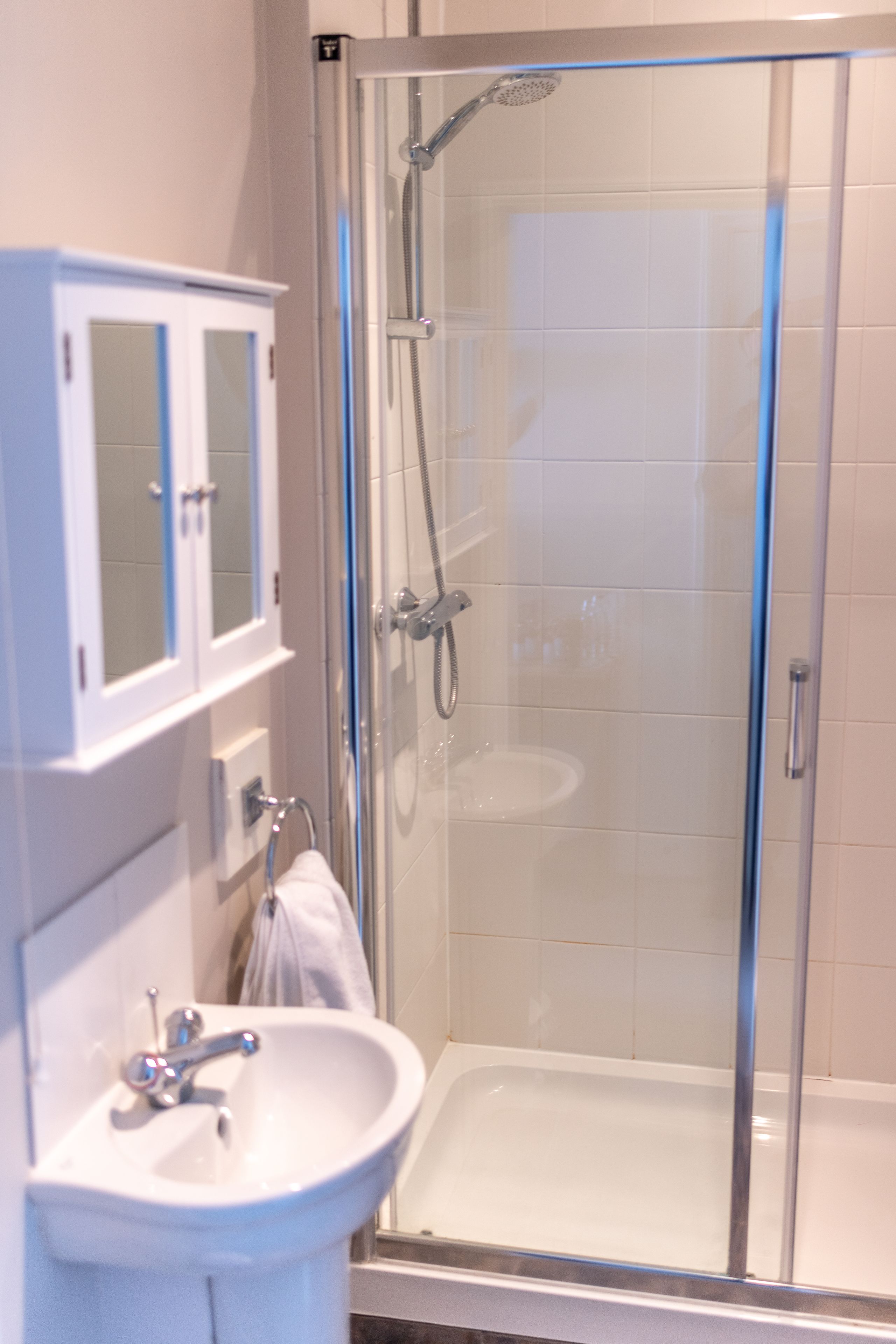 A modern bathroom with a glass-enclosed shower, a white sink, and a cabinet with a mirror.
