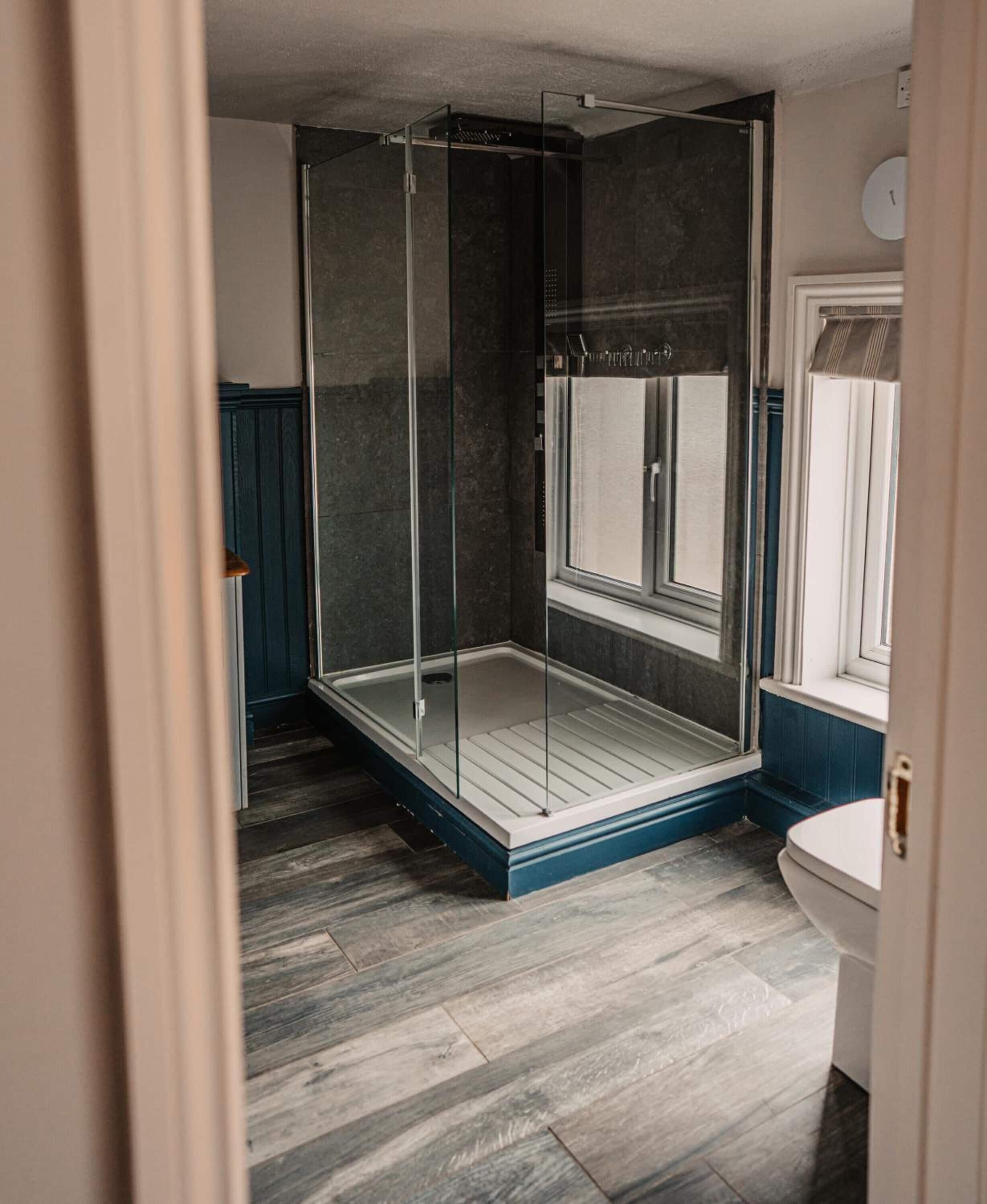 A modern bathroom with a glass-enclosed shower, a toilet, and a window.