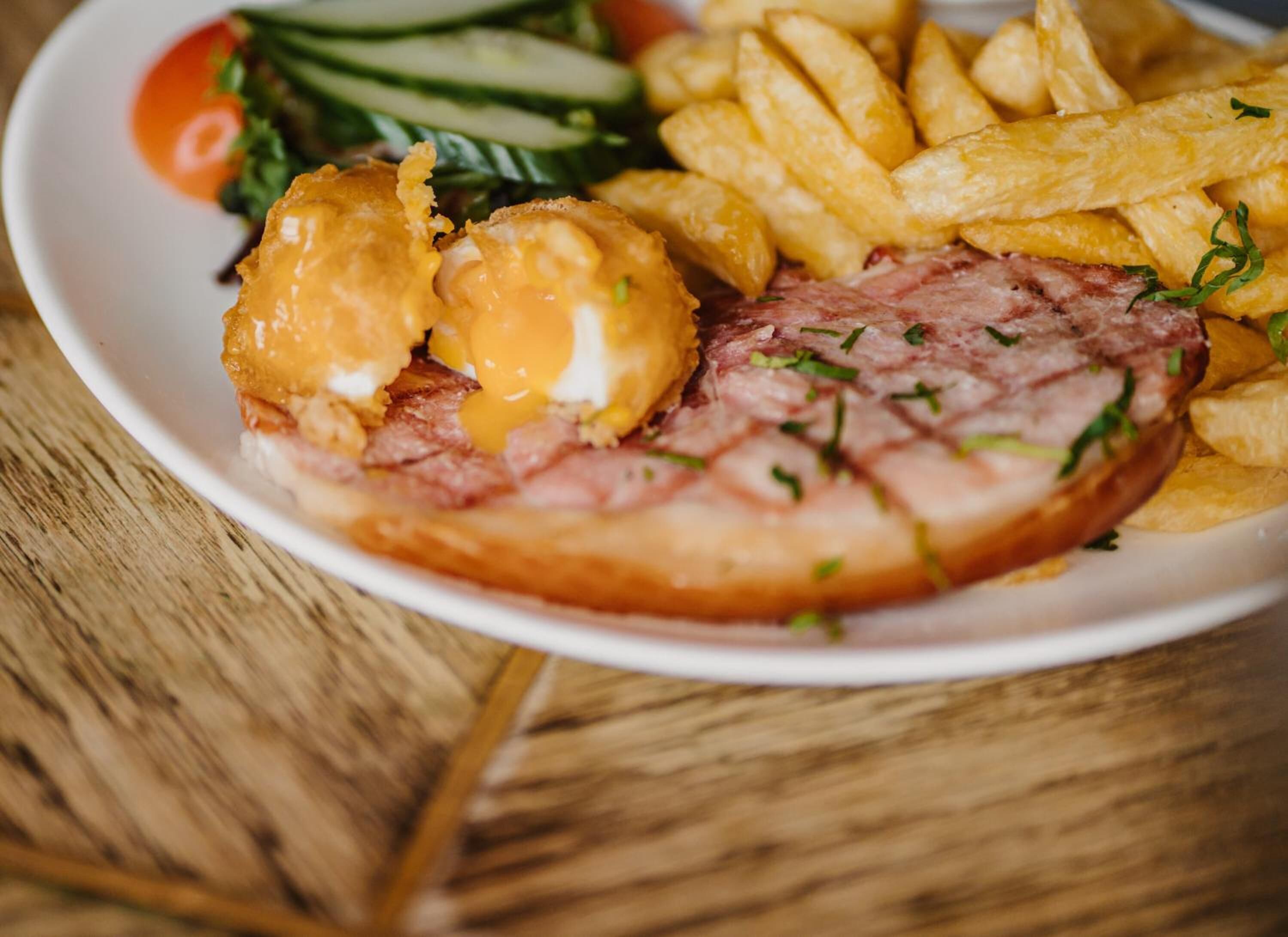 A plate with a slice of ham, a poached egg, and French fries.