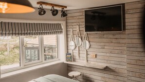 A bedroom with a bed, a TV mounted on the wall, a window with a view, and a shelf with decorative items. - The Ship Inn (Norwich)