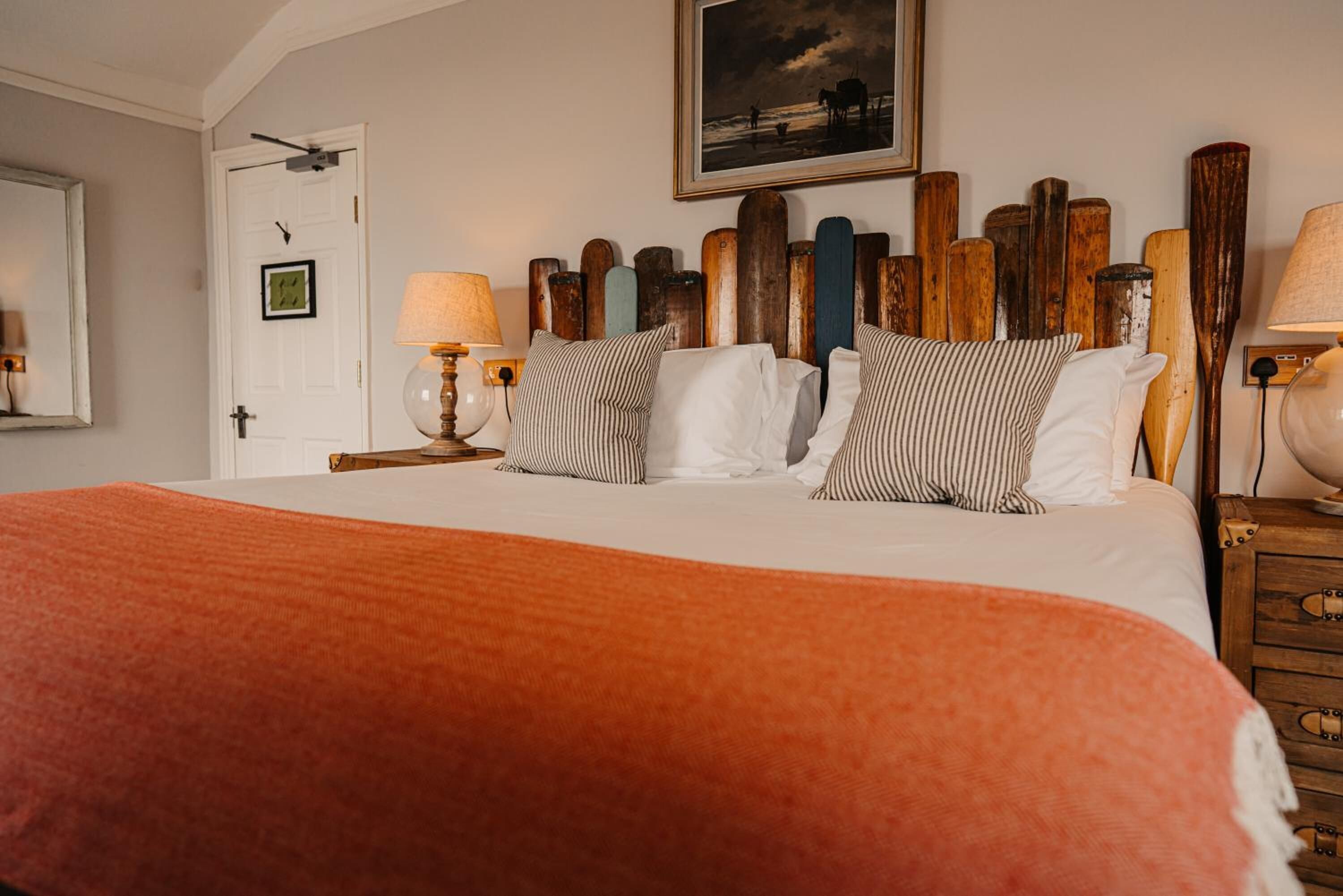 Un dormitorio con cama, almohadas a rayas, cabecera de madera, un cuadro enmarcado en la pared y una puerta con marco.