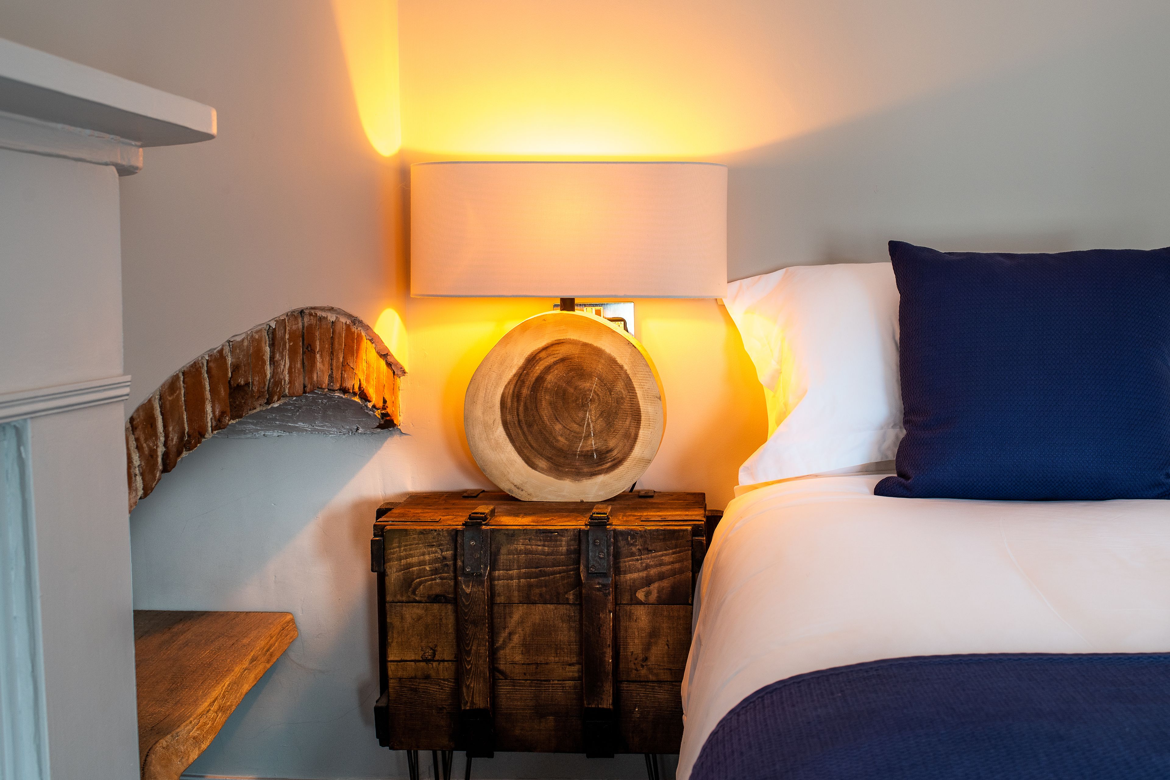 A bedroom with a bed, a wooden chest, a wall-mounted lamp, and a stone wall.