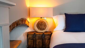 Een slaapkamer met een bed, een houten kist, een wandlamp en een stenen muur.