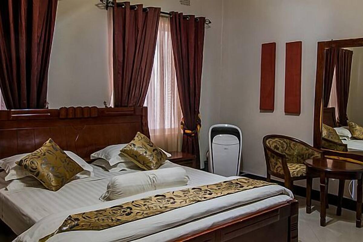 Habitación de hotel con una cama de madera, una mesita de noche, una silla, un escritorio y un espejo.
