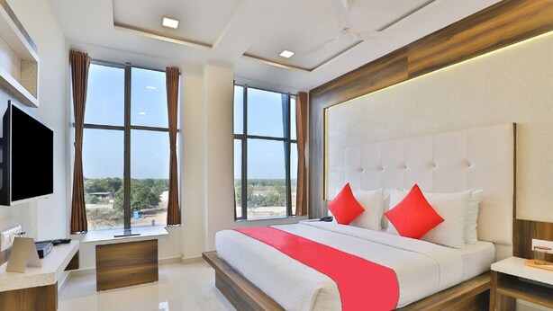 A modern hotel room with a large bed, a flat-screen TV, a desk, and large windows offering a view of the outdoors.