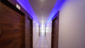A hotel corridor with wooden doors, a tiled floor, and blue underglow lighting.