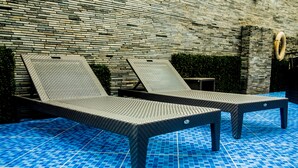 Två solstolar vid en pool med ett kaklat golv och en stenmur i bakgrunden.