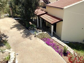 Una zona residenziale con vialetto asfaltato, patio coperto e diverse piante e fiori.