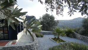 A landscaped garden with a stone pathway, various plants, and a view of distant hills. - Kreta-Auszeit Ferienhaus Anidri (Kantanos-Selino)