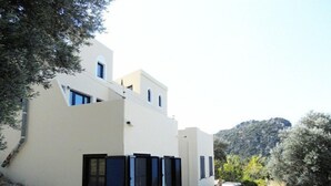 A modern two-story building with a white facade, black shutters, and a stone retaining wall. - Kreta-Auszeit Ferienhaus Anidri (Kantanos-Selino)