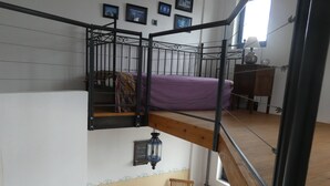 A loft-style room with a bunk bed, a dining table with chairs, a rug, and a hanging lantern. - Kreta-Auszeit Ferienhaus Anidri (Kantanos-Selino)