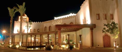 A traditional building with a sign reading "GULF PALACE HOTEL". It features a courtyard with palm trees and a water feature.