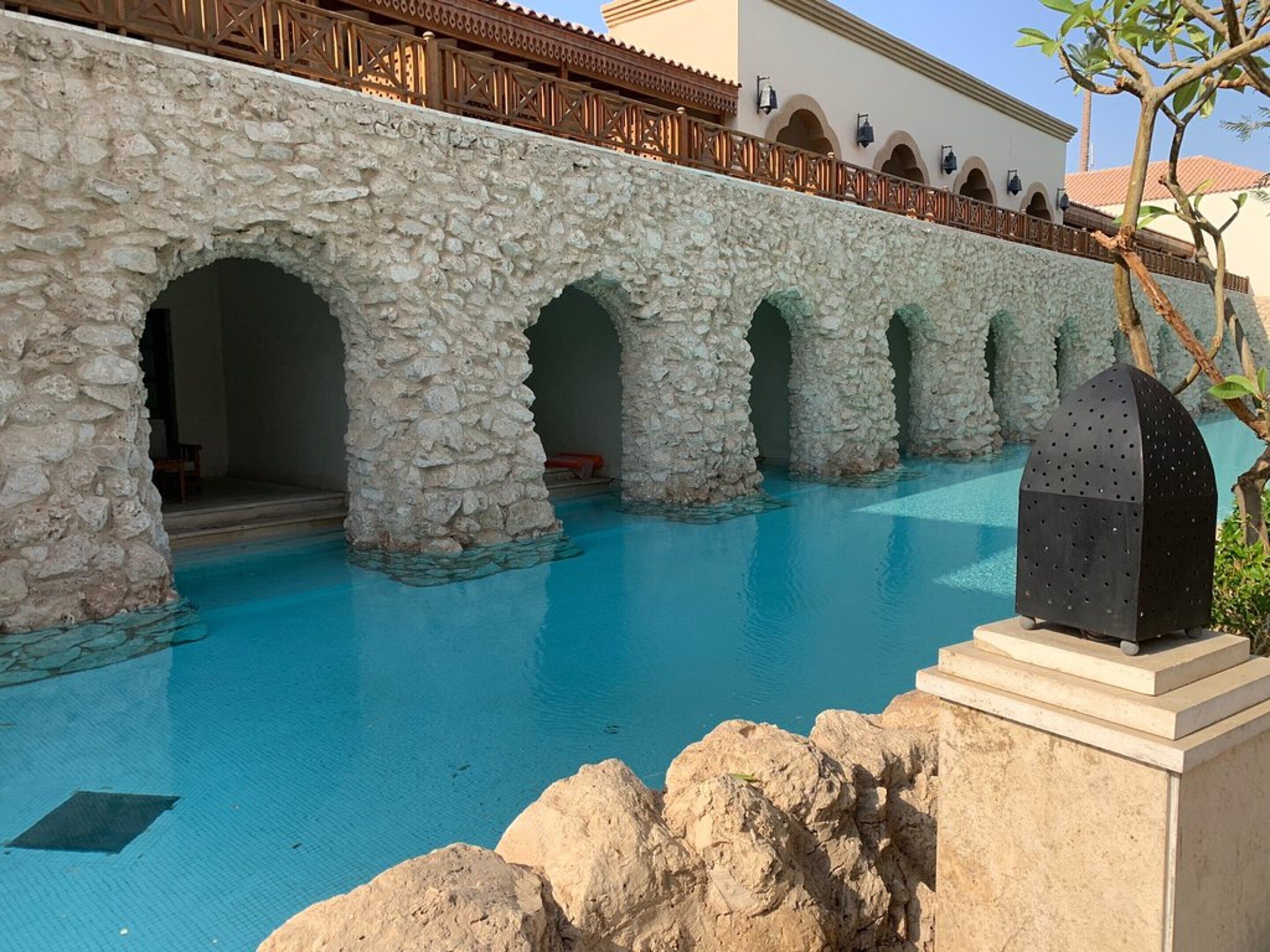 A stone bridge leading to a pool area with a clear blue pool.