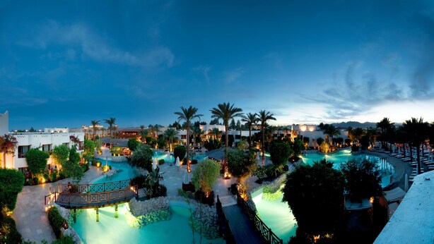 Ein Resort mit mehreren Schwimmbecken, Palmen und einer Brücke, die verschiedene Bereiche miteinander verbindet.