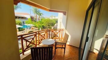 A balcony with a view of a pool and palm trees, a table, and two chairs.