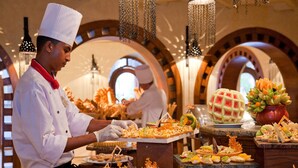 Ein Koch bereitet Essen in einem Restaurant mit gewölbter Decke und dekorativen Kronleuchtern.