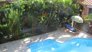 A swimming pool with a tiled deck, surrounded by lush greenery and a few potted plants.