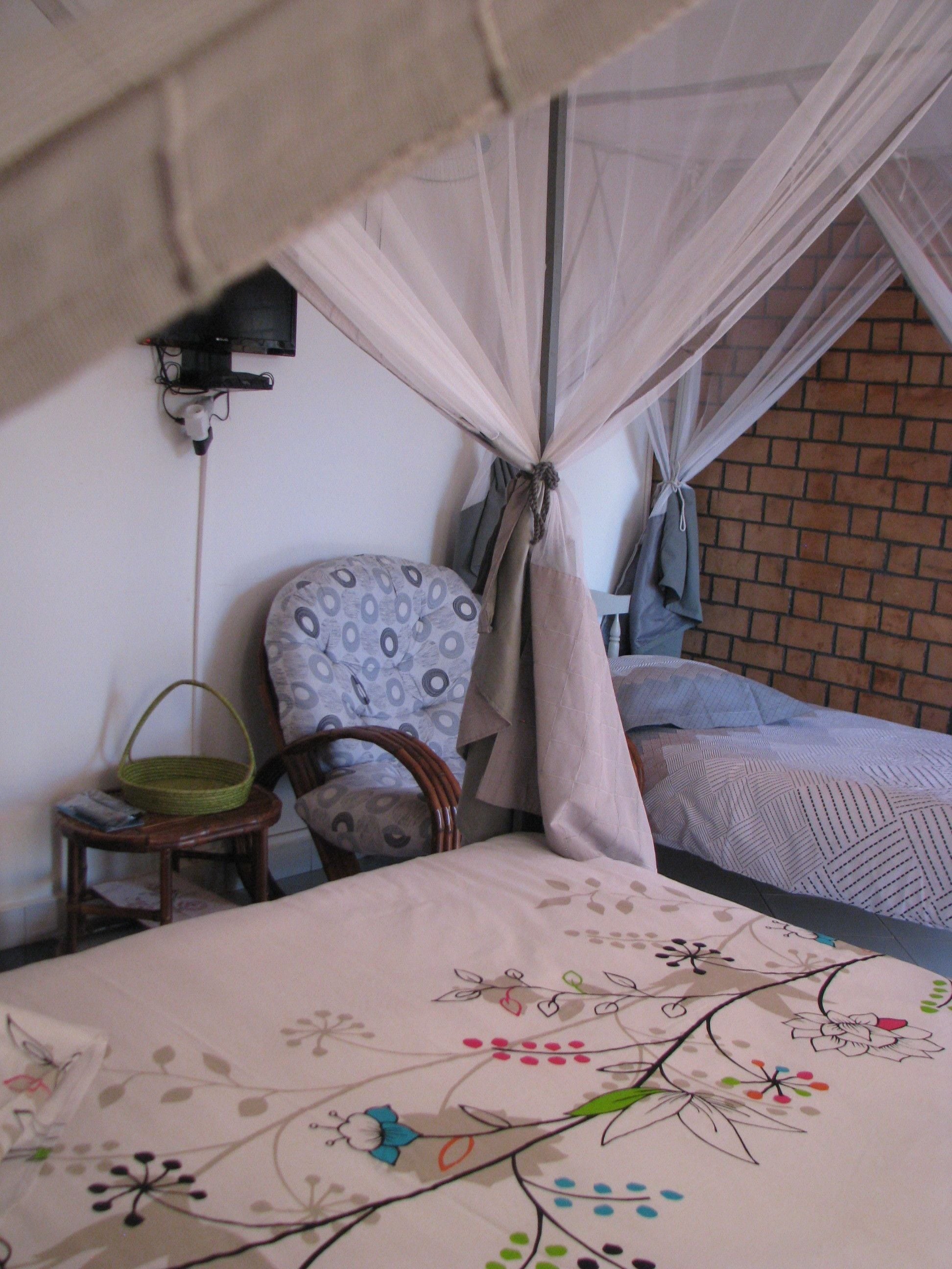 A room with a bed, a chair, a small table with a basket, and a mosquito net over the bed.