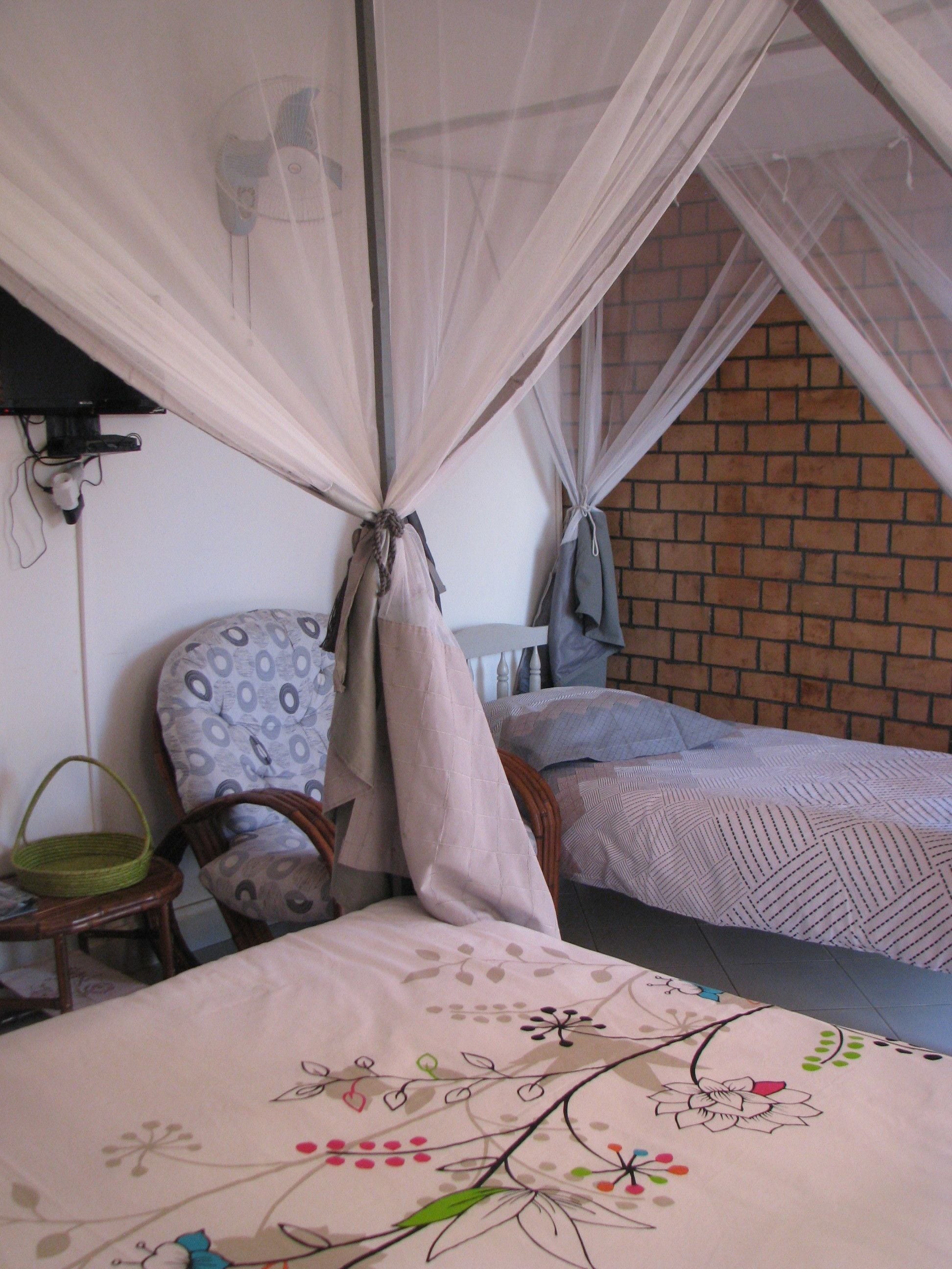 A bedroom with a bed, a chair, and a mosquito net.