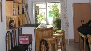 Una habitación con techo alto, una estantería de madera, una mesa de comedor con sillas, una lámpara colgante de mimbre y vistas a través de una ventana con puerta.
