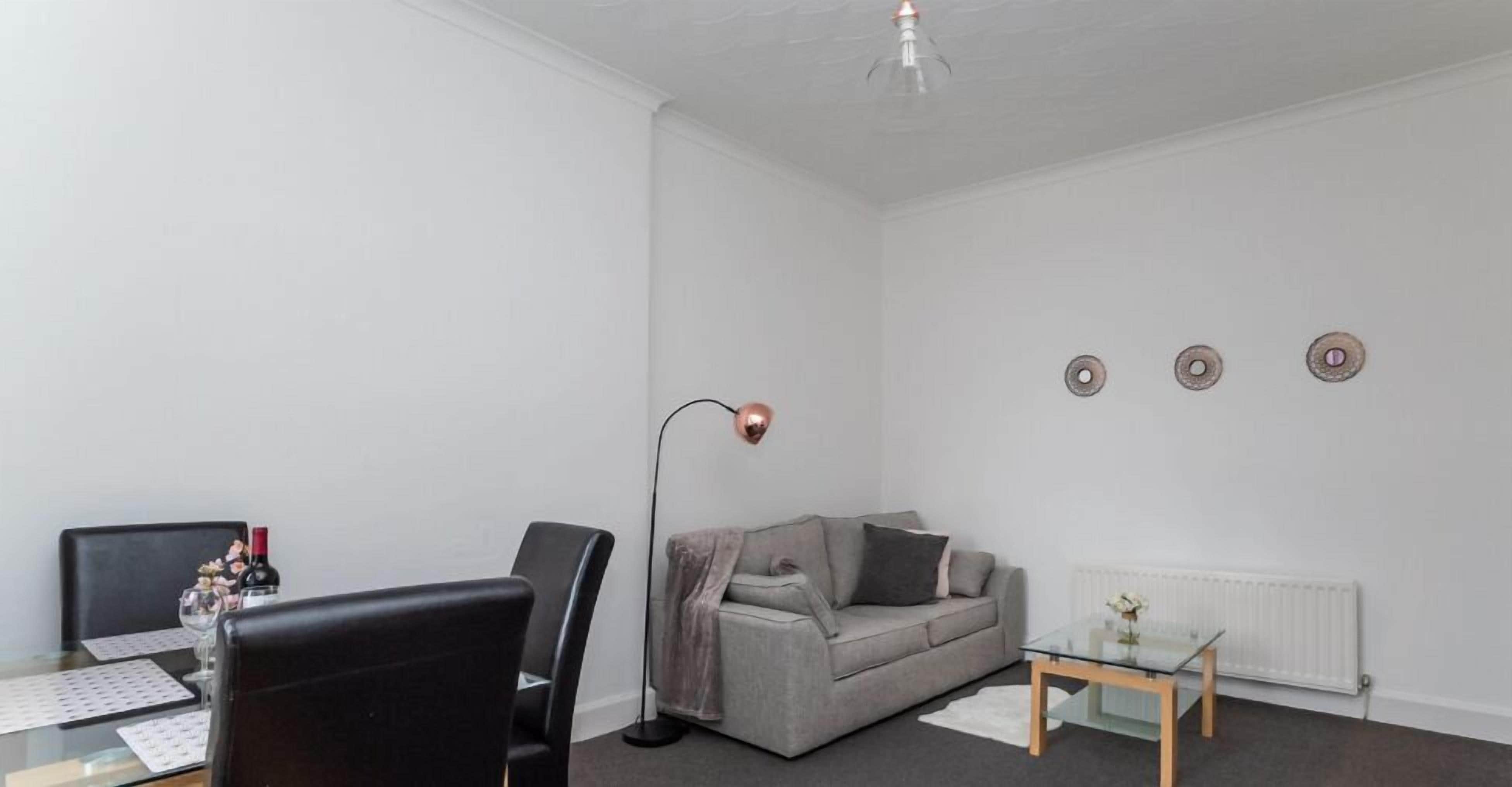 Una sala de estar moderna con un sofá gris, sillas negras, una mesa de centro de vidrio y una lámpara de pie.