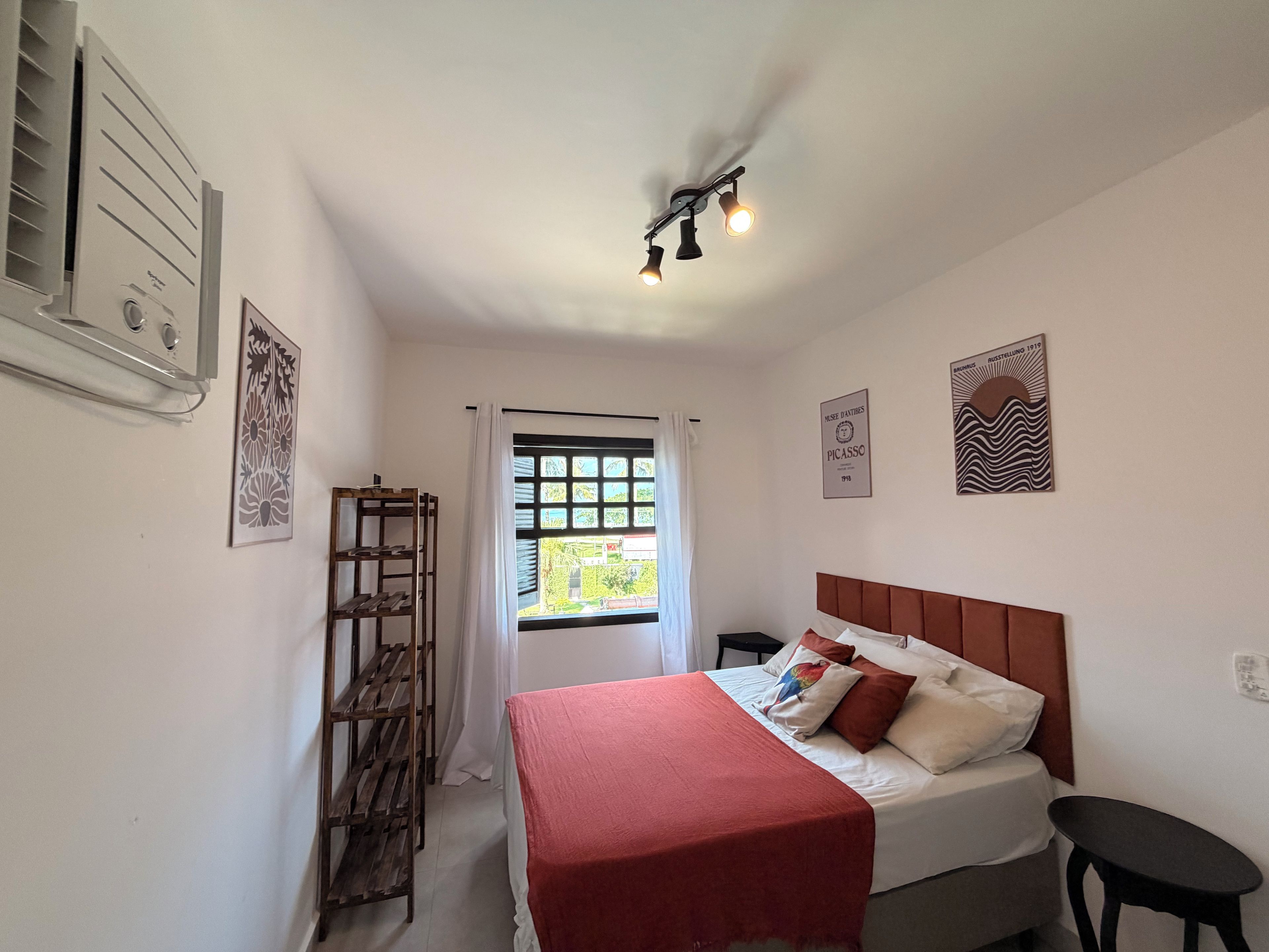 Un dormitorio con cama, mesita de noche, estante de madera, ventana con cortinas y decoración en la pared.