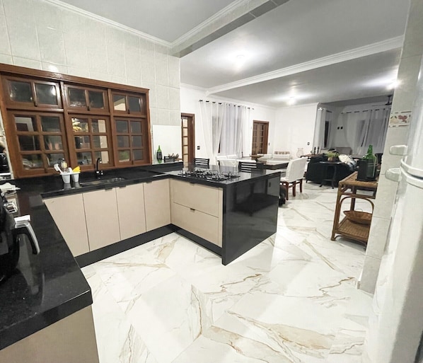 A modern kitchen with a marble floor, wooden cabinets, and a central island. - Beachfront house with pool for up to 20 people. (Bertioga)