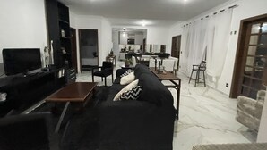 Ein modernes Wohnzimmer mit einem schwarzen Sofa, einem Fernseher und einem Essbereich mit Stühlen und einem Tisch.