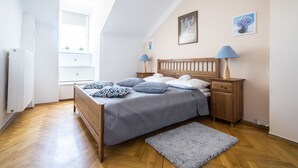 Ein Schlafzimmer mit einem hölzernen Bett, einem Nachttisch, zwei Wandleuchten und einem Fenster mit Blick auf Grünflächen.