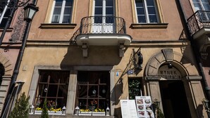 Ein Gebäude mit einem zentralen Eingang, zahlreichen Fenstern und einem Balkon mit Geländern.