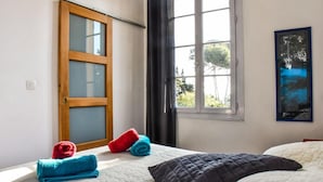 A bedroom with a bed, a window with curtains, a door with a frosted glass panel, and a framed picture on the wall. - Escale au soleil Hôtel et Appartement (Fréjus)