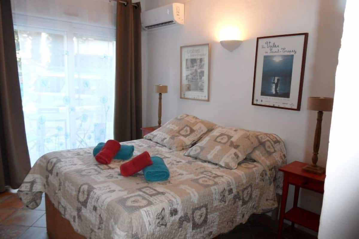 Une chambre à coucher avec un lit, deux lampes fixées au mur, un tableau encadré et une fenêtre avec des rideaux.