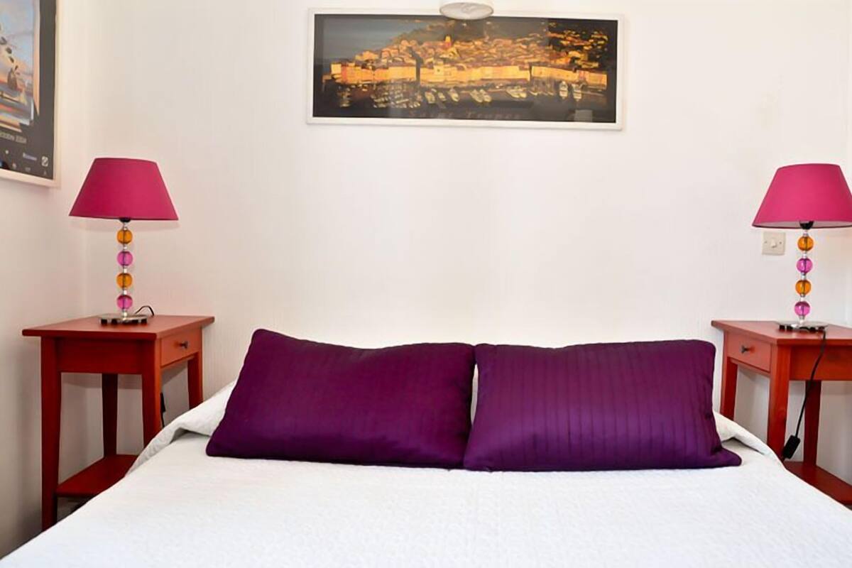 Une chambre d’hôtel avec un lit, deux tables de chevet, deux lampes et un tableau encadré au mur.