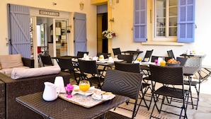 A reception area with a sign, wicker furniture, and a table set with breakfast items. - Escale au soleil Hôtel et Appartement (Fréjus)
