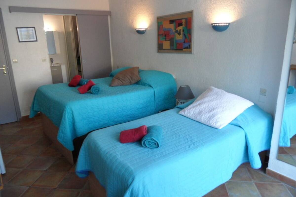 Une chambre avec deux lits, chacun recouvert d’une couverture bleue et agrémenté d’oreillers, une petite table avec une lampe et un tableau accroché au mur.