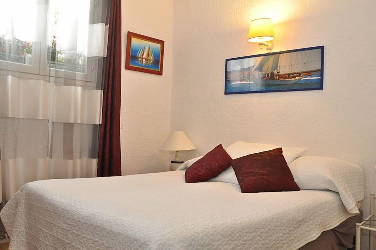 Une chambre d’hôtel avec un lit, deux oreillers, une table de chevet, une lampe et deux tableaux au mur.