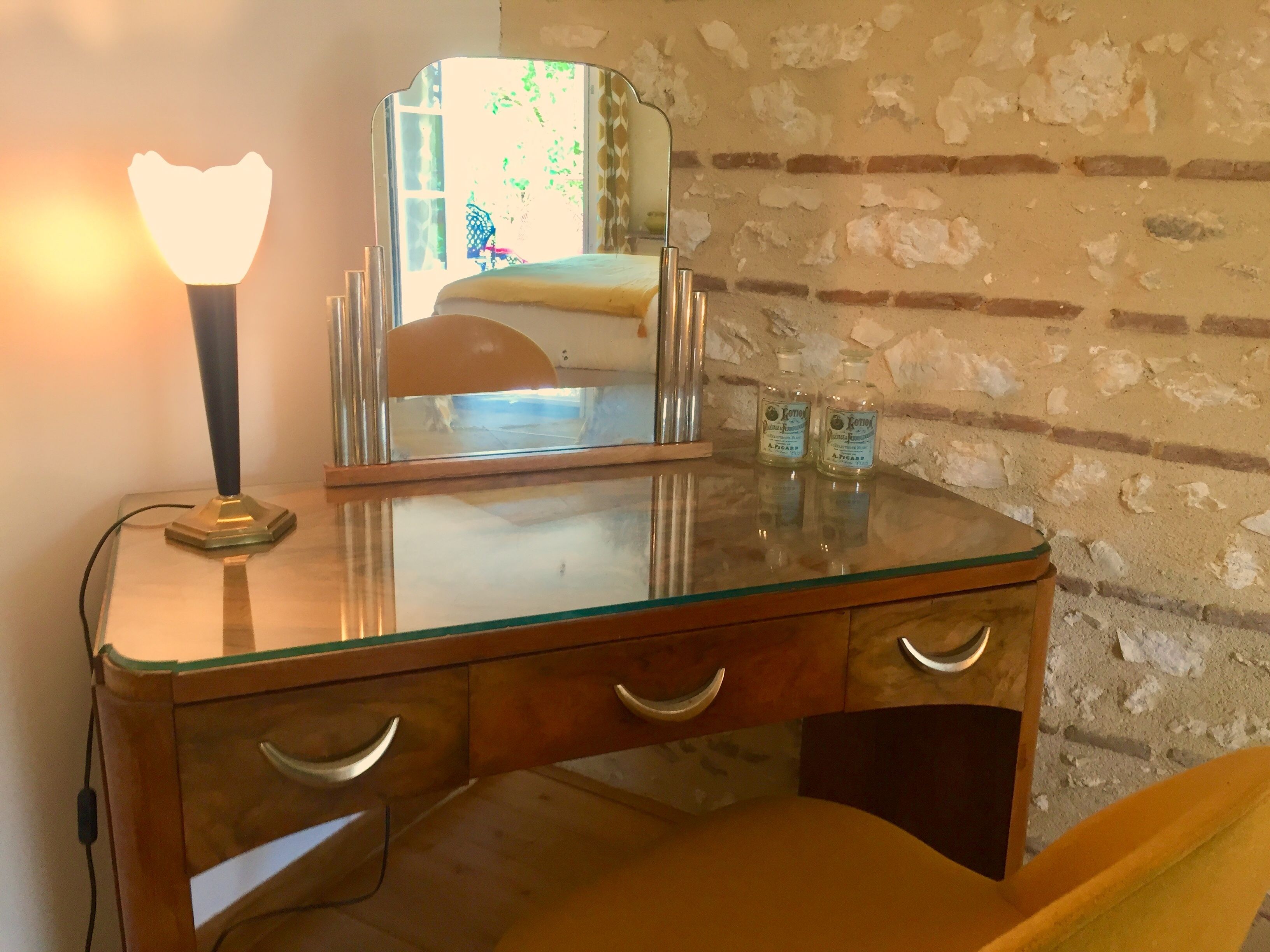 Une commode en bois avec un plateau en verre, un miroir et deux bouteilles étiquetées « Koton ».