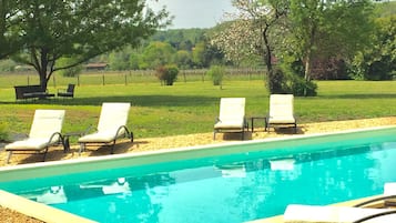 Una piscina con cuatro sillas de descanso alineadas a lo largo de su borde, rodeada por una zona de grava.