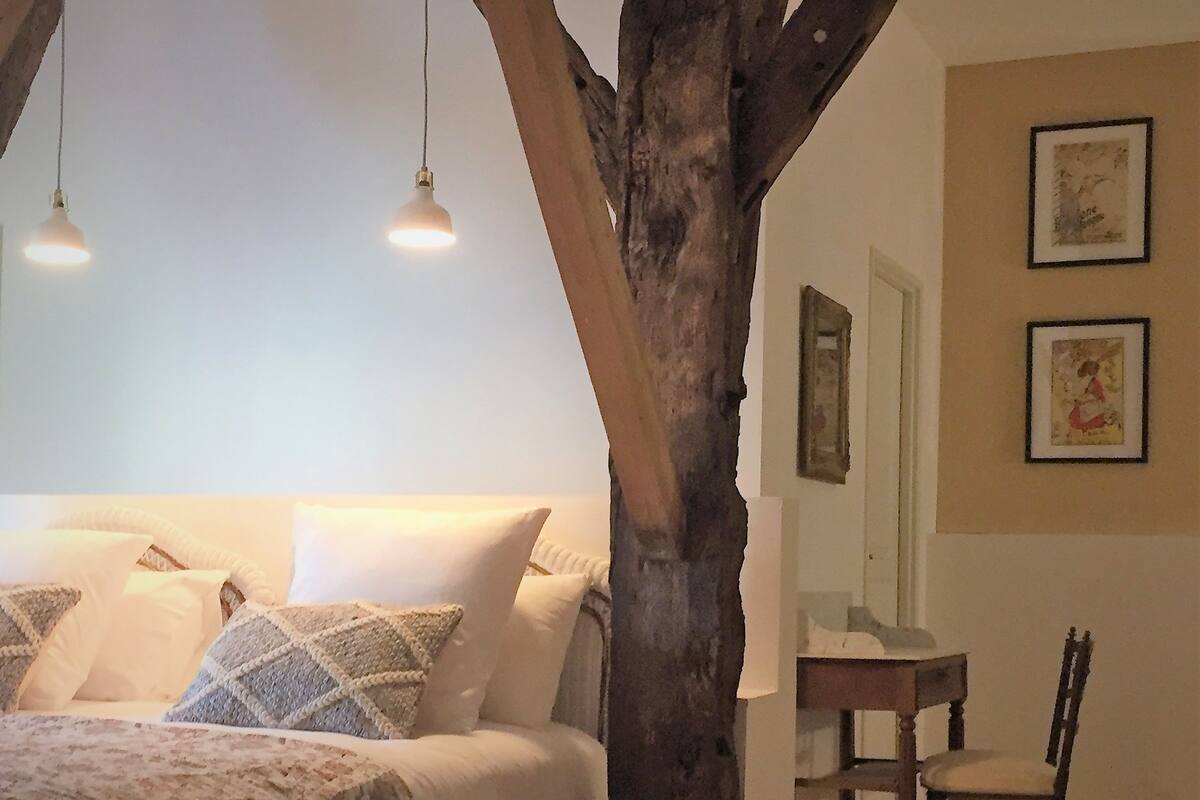 Un dormitorio con una cama grande, dos lámparas colgantes, un tronco de árbol de madera y dos cuadros en la pared.