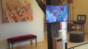Une pièce avec un banc en bois, un téléviseur fixé sur un pilier sombre et un grand tableau abstrait accroché au mur.